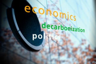 Text "economics" in orange, "decarbonization" in green, and "politics" in white on a blurred background with abstract elements.