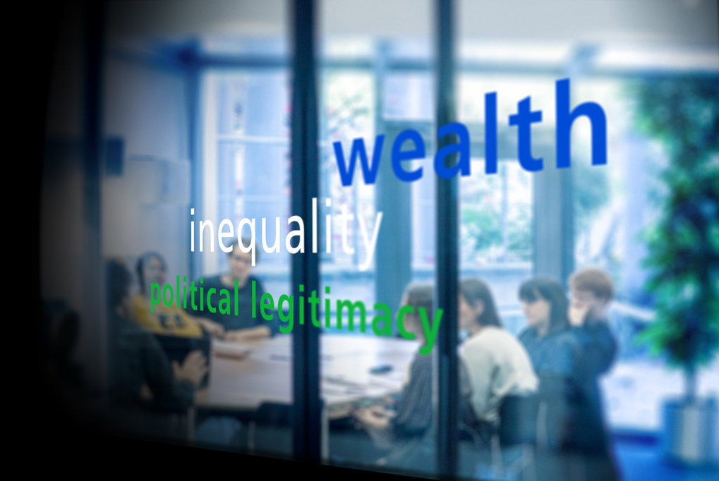 Glass pane displays words wealth, inequality, political legitimacy; meeting in background with people partially visible.