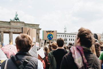 Eine Gruppe von Demonstranten versammelt sich mit Umweltschutz-Plakaten vor dem Brandenburger Tor. Im Hintergrund ist eine Skulptur zu sehen.