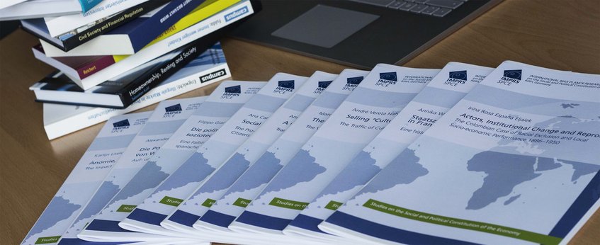 Ein Schreibtisch mit Berichten über institutionellen Wandel, daneben ein Laptop und gestapelte Bücher.