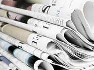 Ein Stapel gefalteter Zeitungen zeigt verschiedene Überschriften und Bilder in einer Mischung aus Farbe und Schwarzweiß, die Details von Schlagzeilen und Artikeln erkennen lassen.