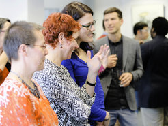 Attendees converse at a professional event; one person gestures with raised hand, wearing patterned clothing, surrounded by others.