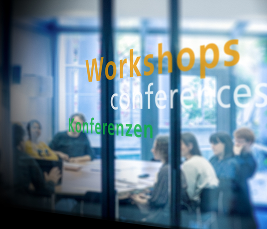 Illustrative blurred image, keywords "Workshops," "conferences," and "Konferenzen" in the foreground