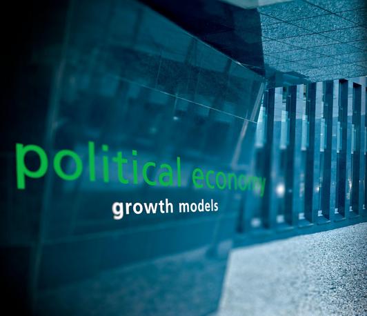 Illustratives Bild mit "political economy" und "growth models" Schriftzügen im Vordergrund; im Hintergrund ein Gebäude (leicht verschwommen)